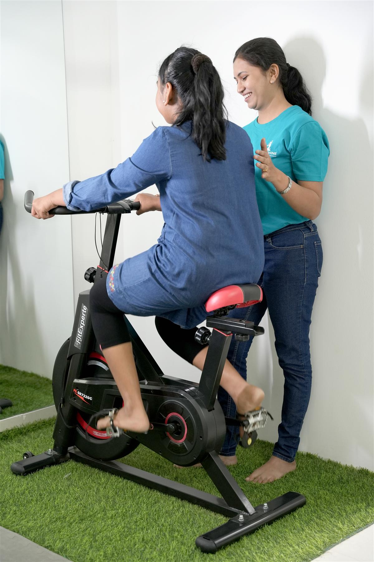 PhysioShine therapist guiding a child on an exercise bike during a pediatric rehabilitation session